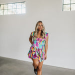 Front view of Elisabeth Romper with allover abstract print, flowy mini skirt, wide straps, and bustier button up front.