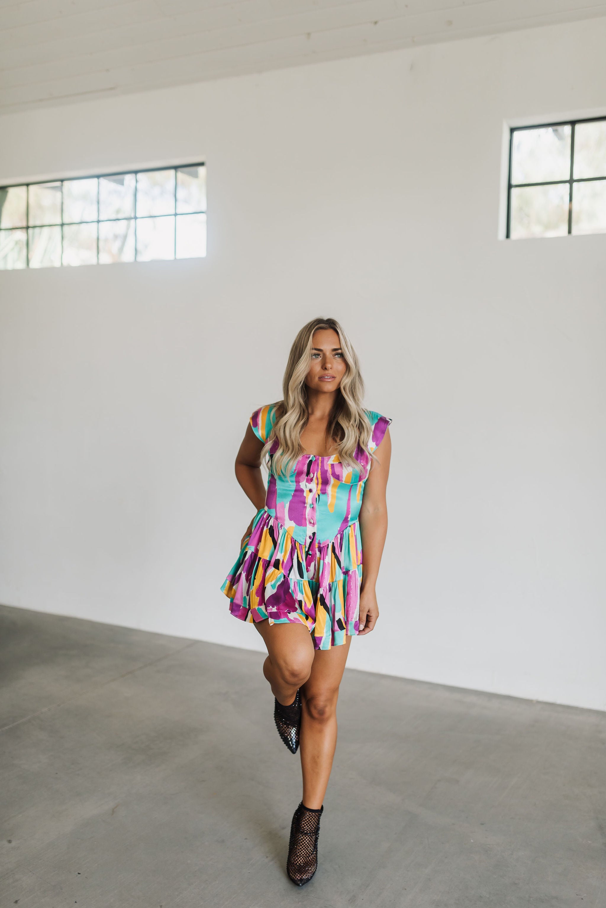 Front view of Elisabeth Romper with allover abstract print, flowy mini skirt, wide straps, and bustier button up front.