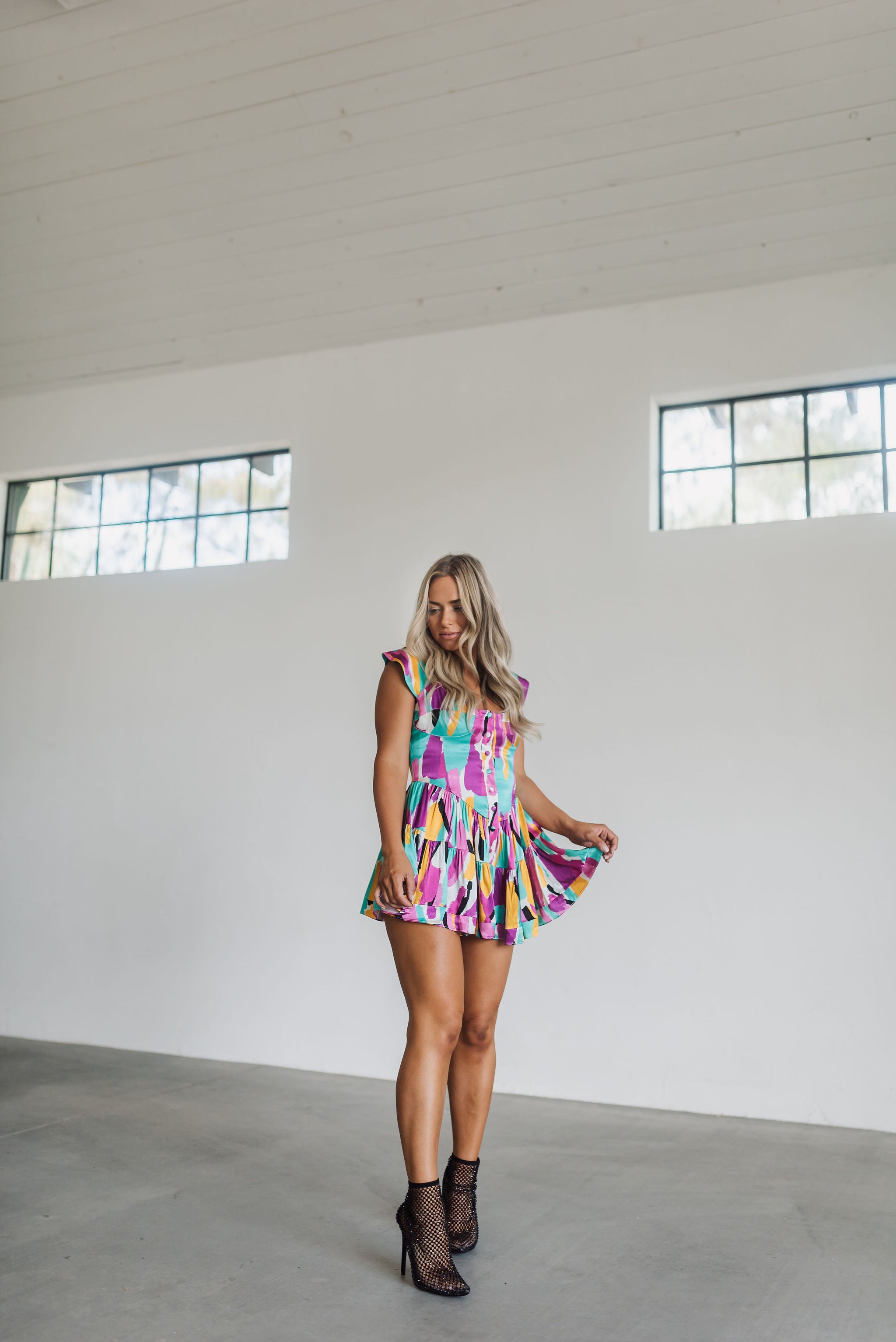 Front angled view of Elisabeth Romper with allover abstract print, flowy mini skirt, wide straps, and bustier button up front.