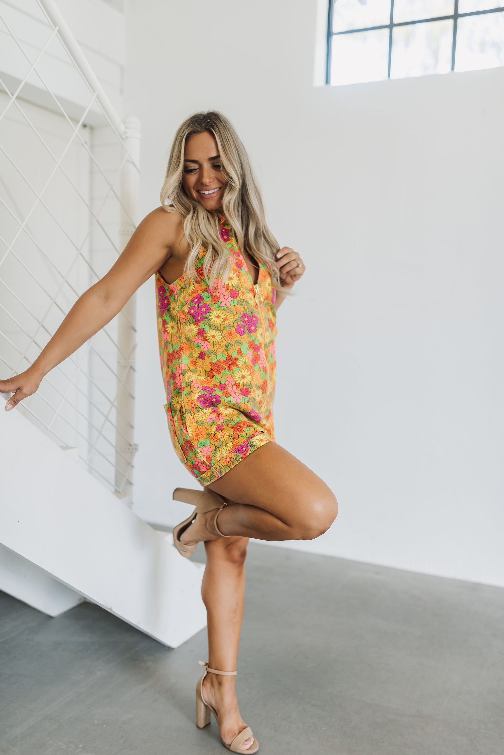 Side view of Reno Romper in allover neon floral print with sleeveless zip up front and collar neck.