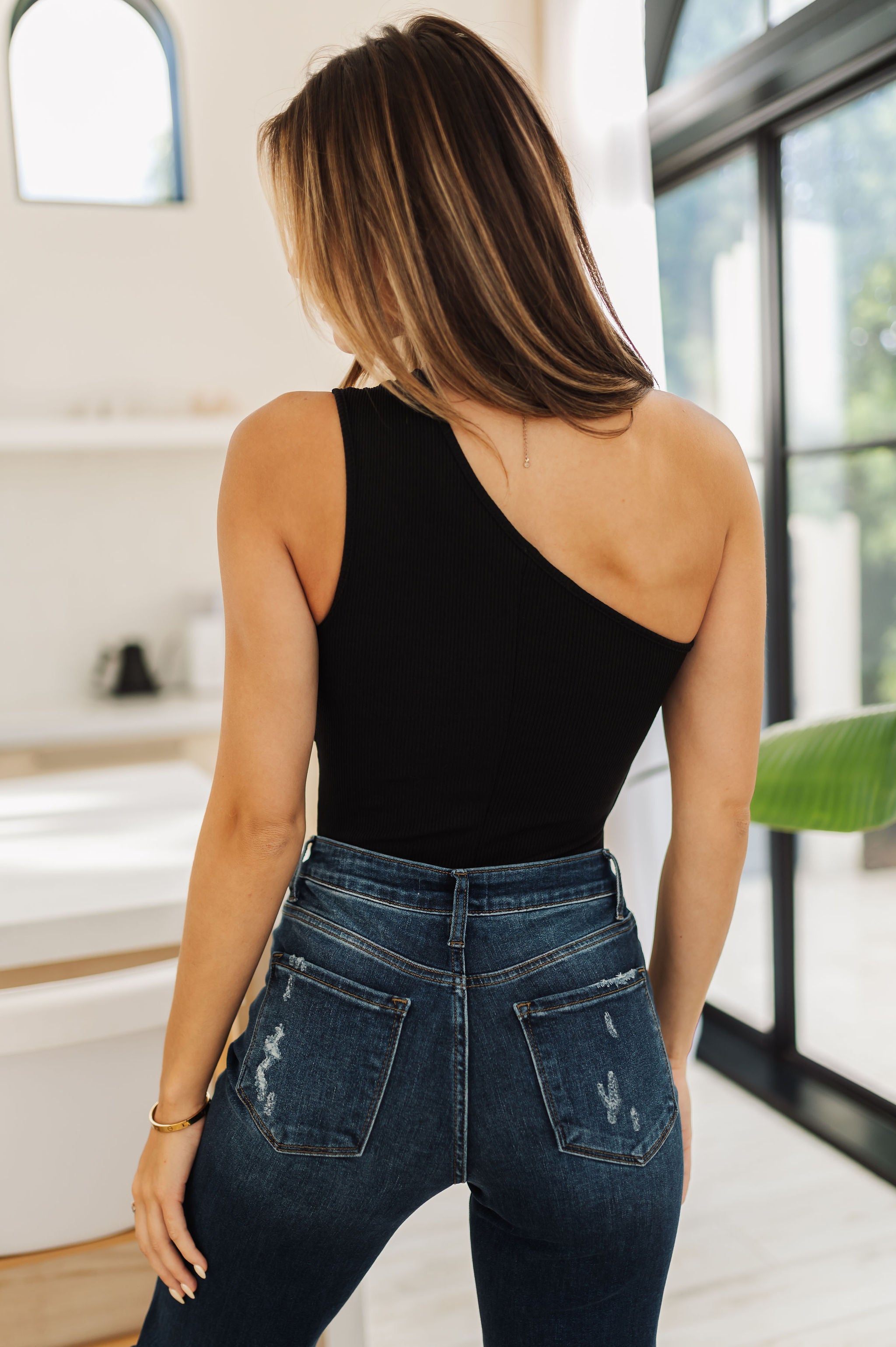 Rear view of Sleeveless Cut Out Body Suit in black with one shoulder strap. 