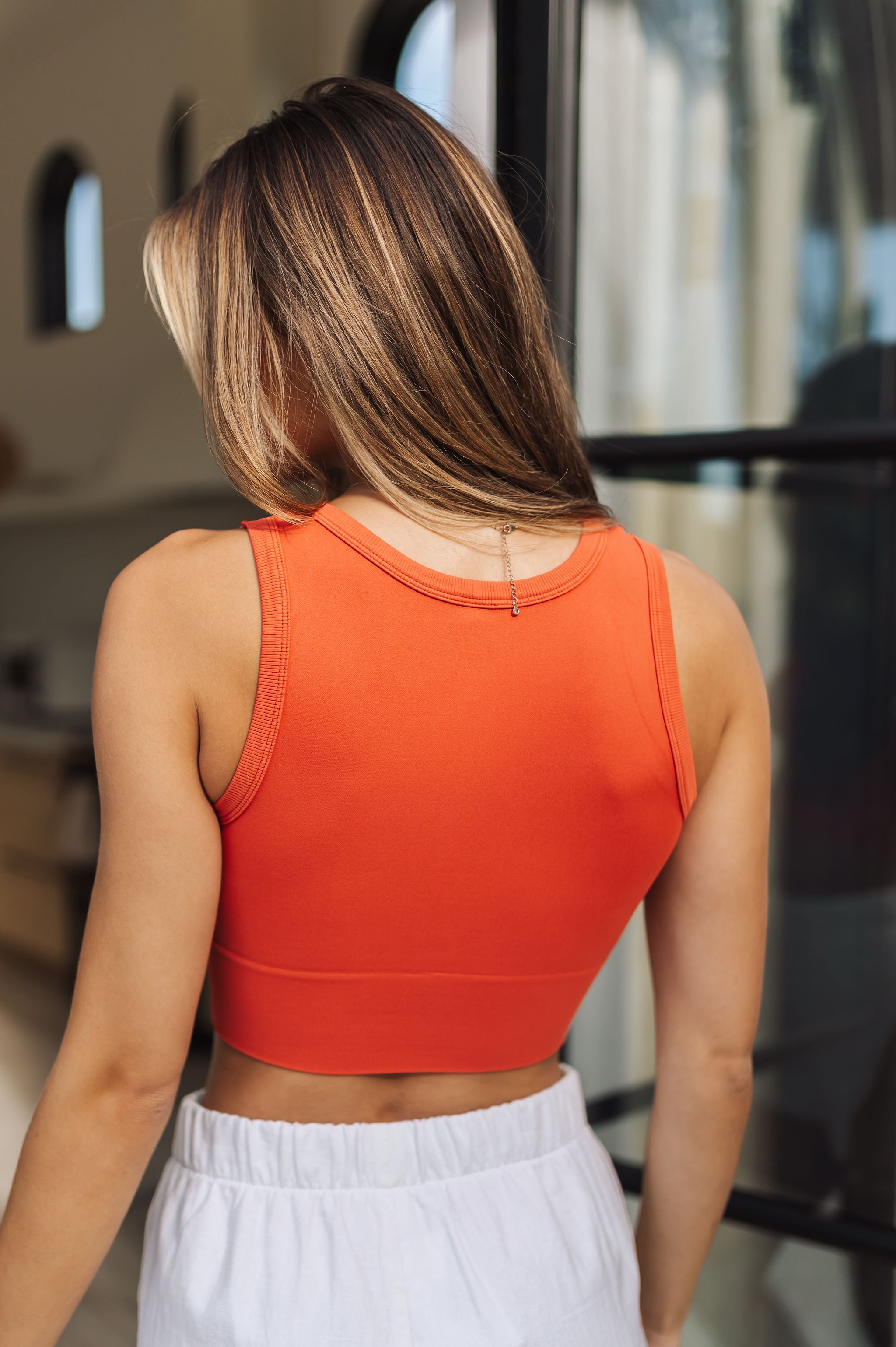 Rear view of Deep Scoop Crop Top in a burnt sienna color with banded hem. 