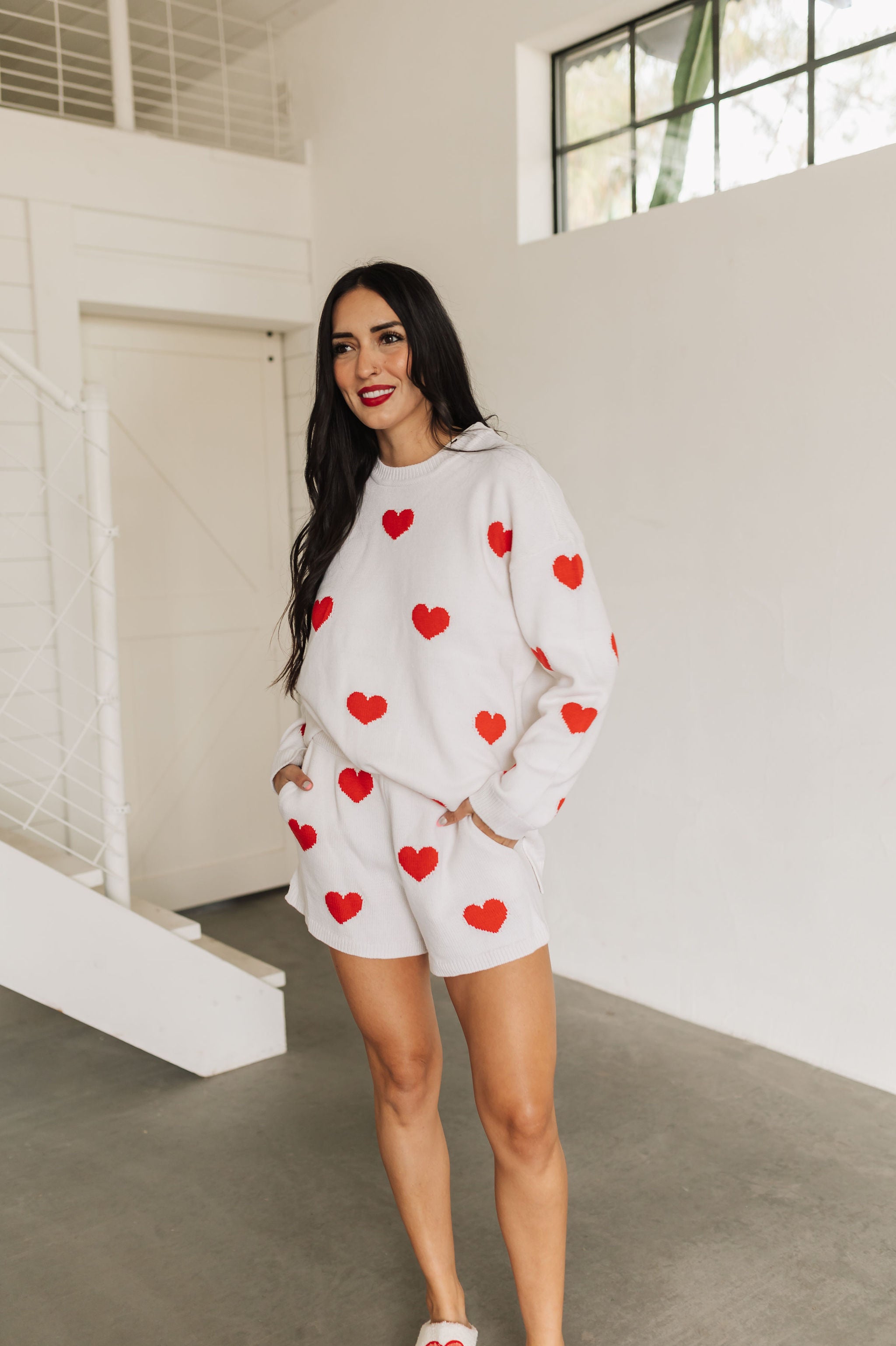 Front angled view of white crewneck Go To Sweater with red hearts print and ribbed hemline. 