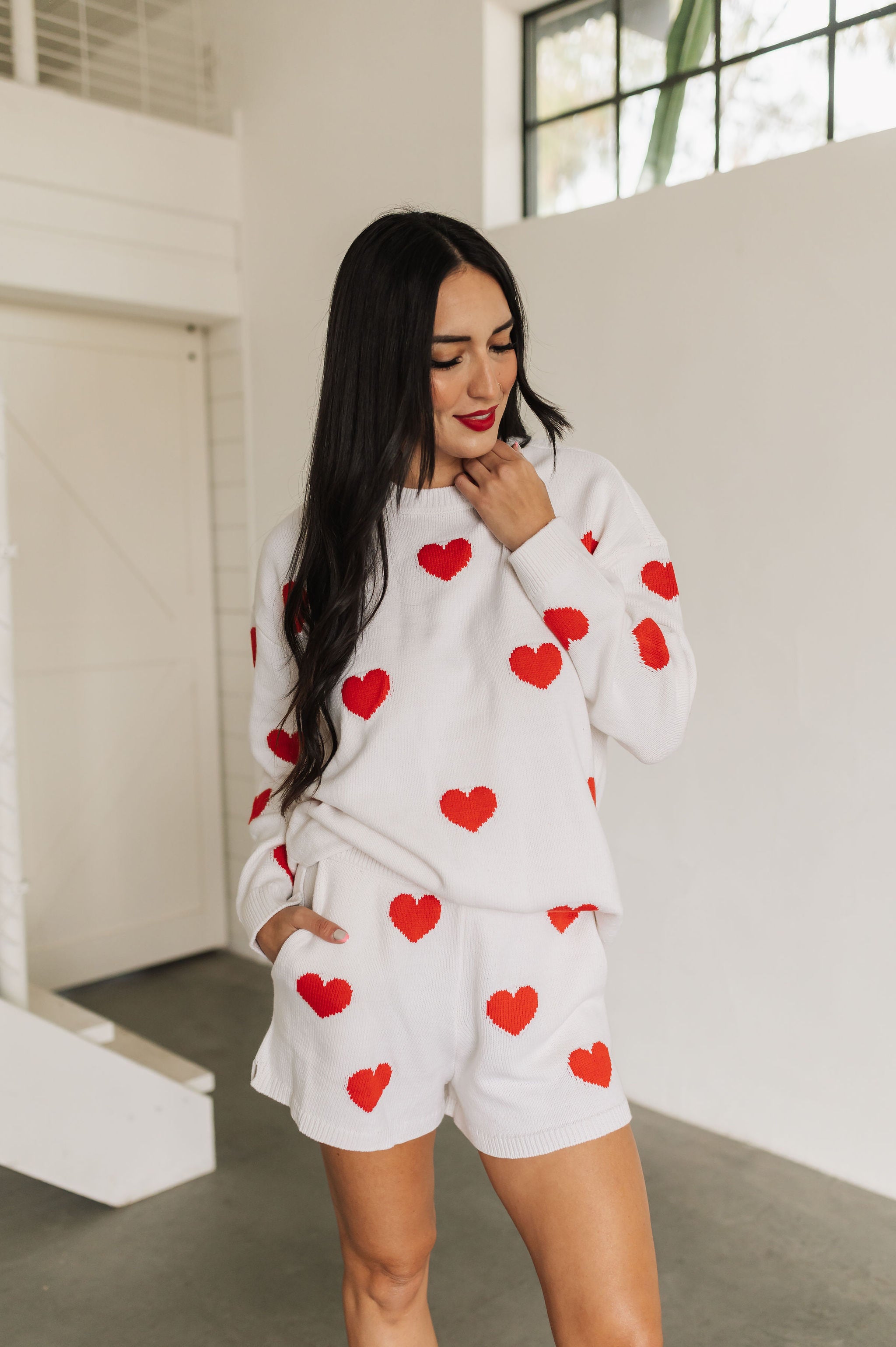 Front view of white crewneck Go To Sweater with red hearts print and ribbed hemline. 
