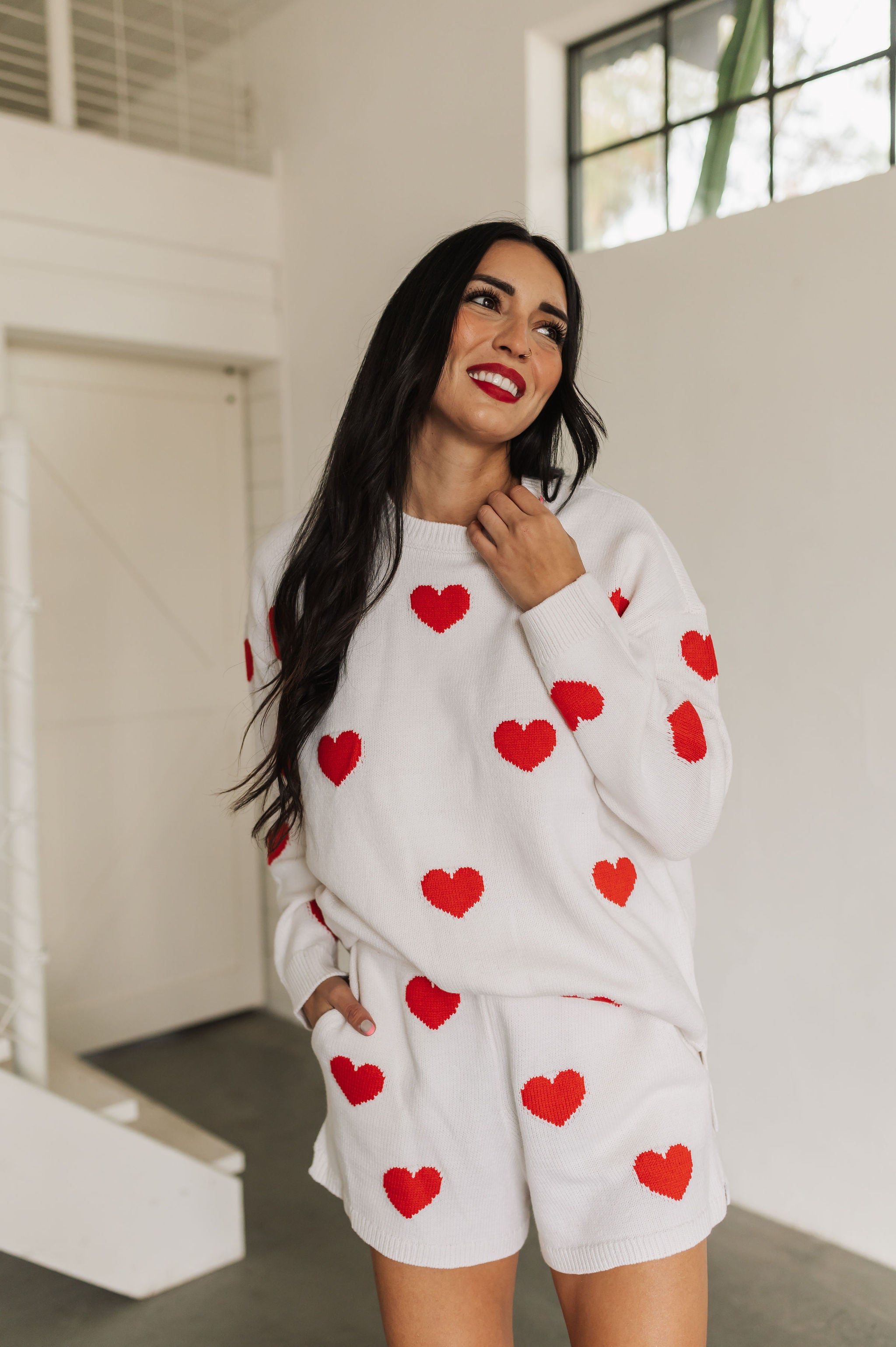 Front view of white crewneck Go To Sweater with red hearts print and ribbed hemline. 
