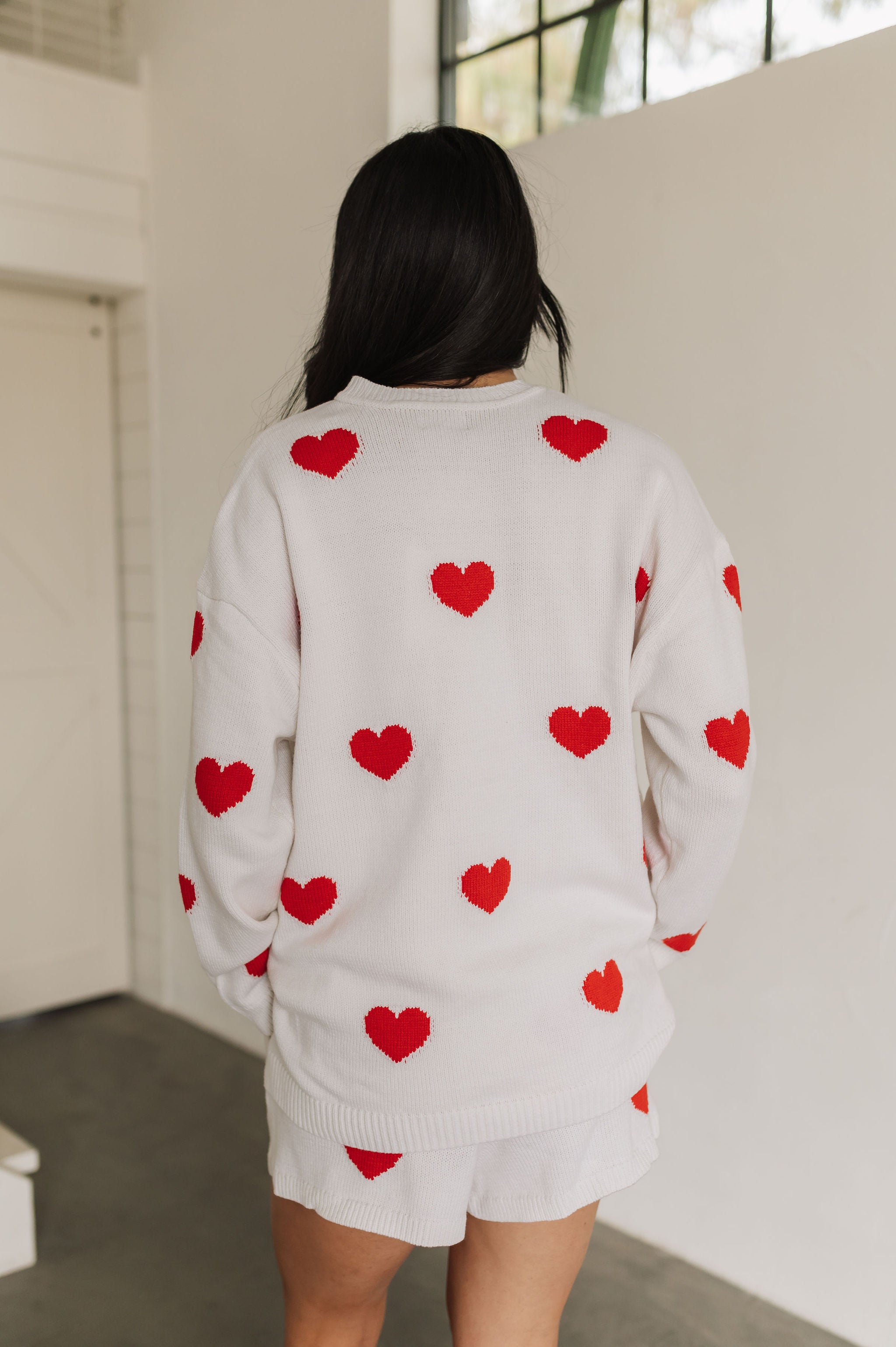 Rear view of white crewneck Go To Sweater with red hearts print and ribbed hemline. 