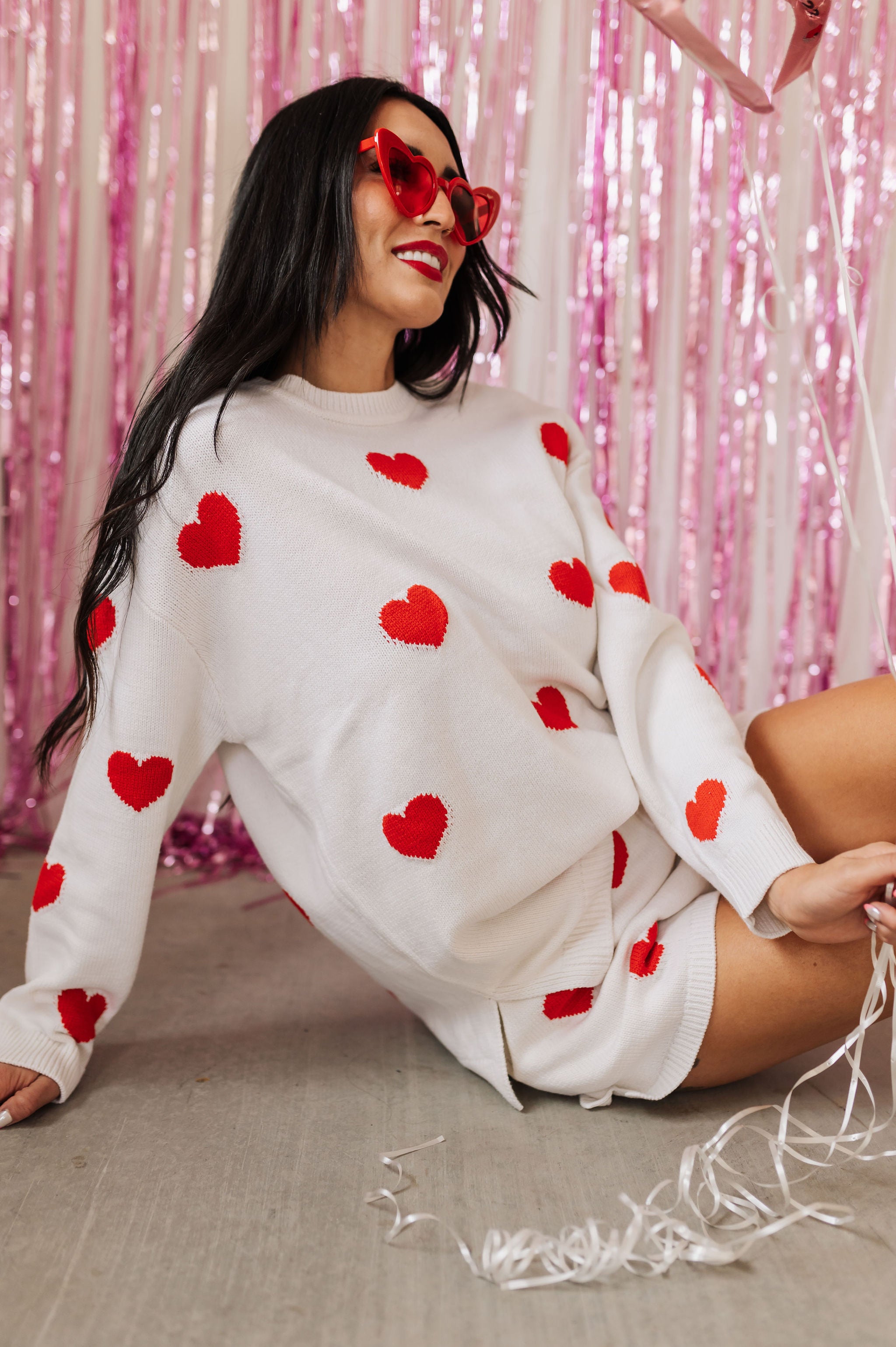 Front angled view of white crewneck Go To Sweater with red hearts print and ribbed hemline. 