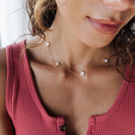 Close-up of a woman wearing a pink ribbed tank top and a delicate necklace with small stones.