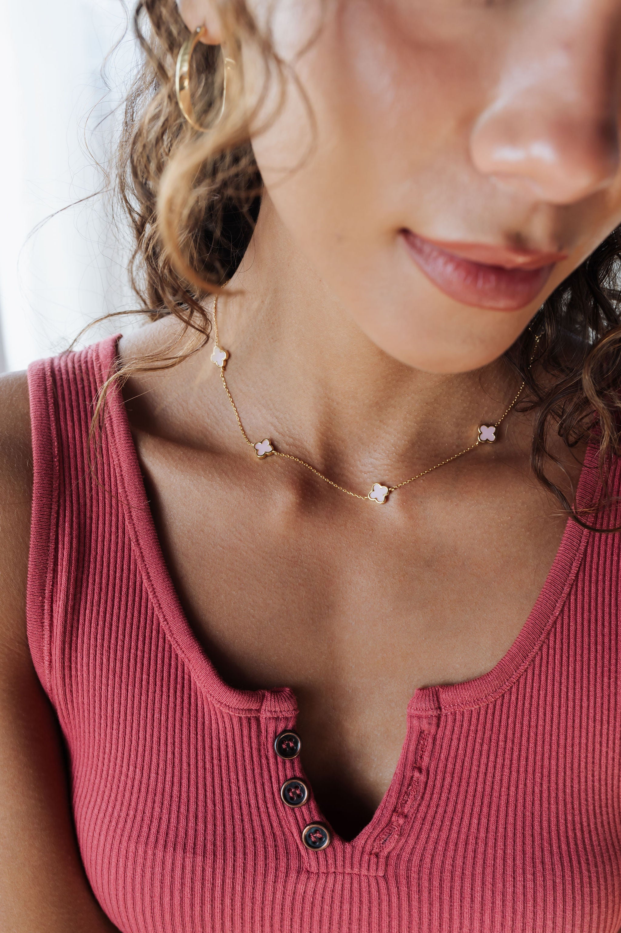 Close-up of a woman wearing a pink ribbed tank top and a delicate necklace with small stones.