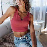 Woman wearing a red crop top and blue jeans sitting on a couch in a bright room.