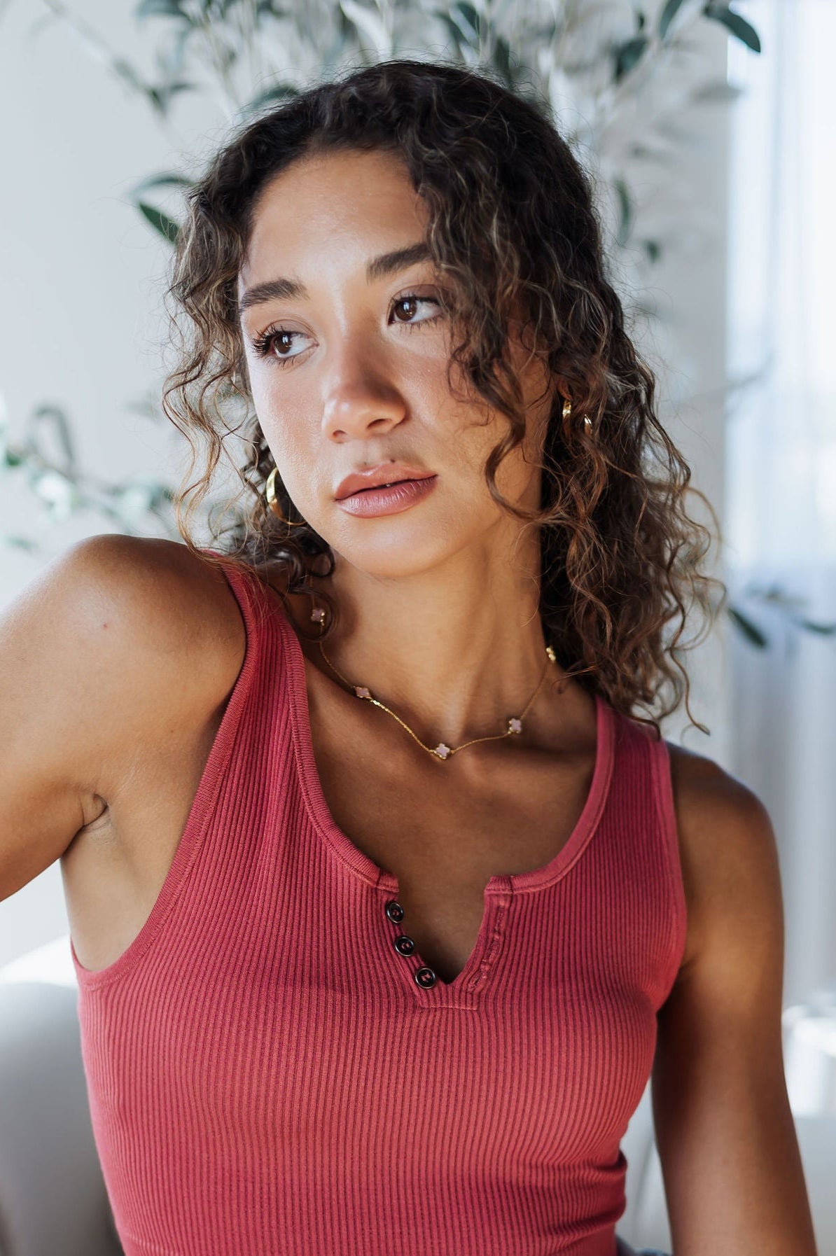 Woman wearing a red crop top and blue jeans sitting on a couch in a bright room.