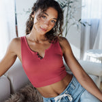 Woman wearing a pink tank top and light blue jeans sitting on a couch.