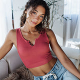 Woman wearing a pink tank top and light blue jeans sitting on a couch.