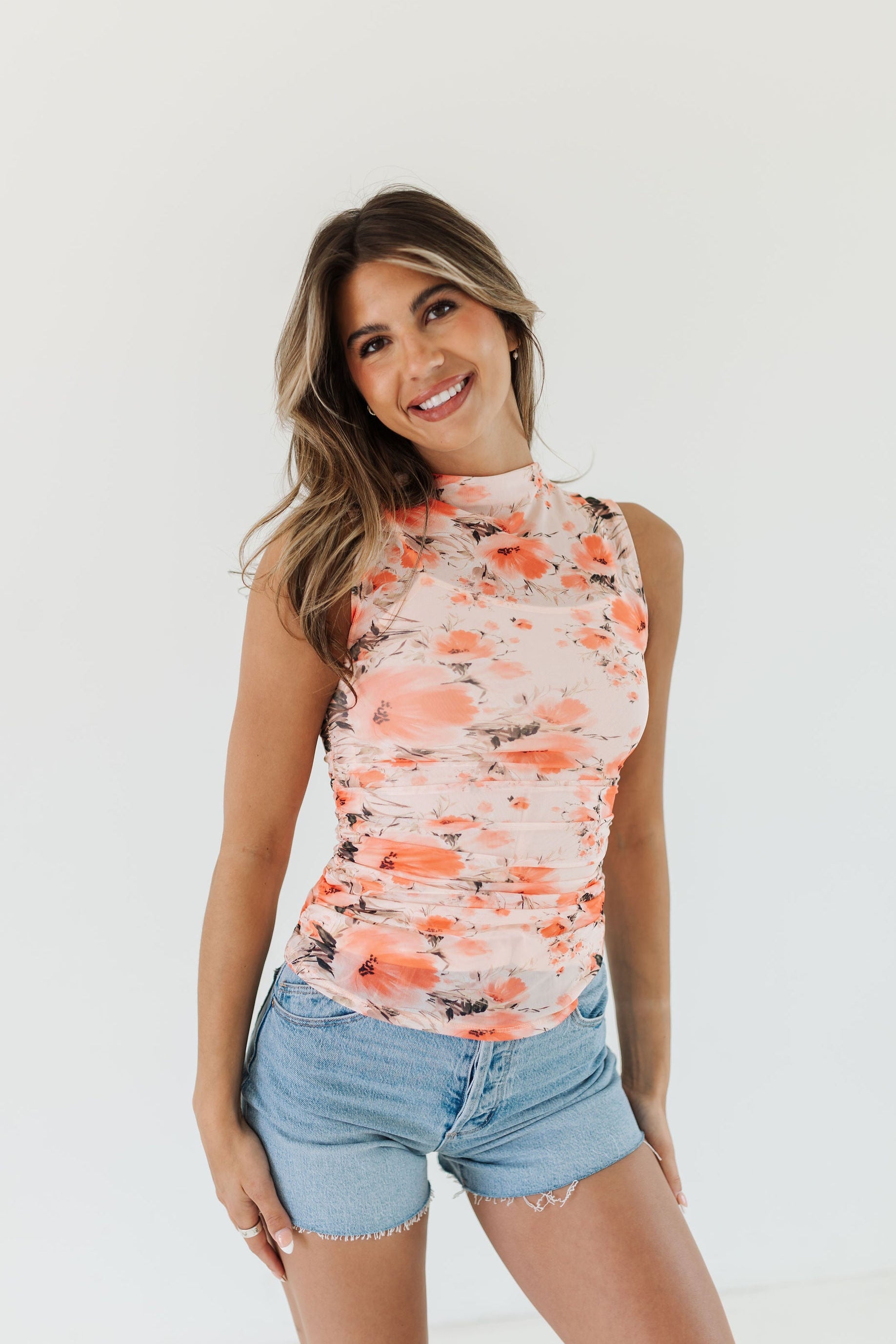 Woman wearing a floral sleeveless top and denim shorts on a white background