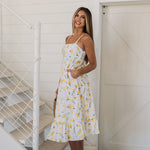 Side view of Summer Fling Midi Dress with embroidered Limoncello print, thin straps, square neckline, side pockets, and ruffled hem.