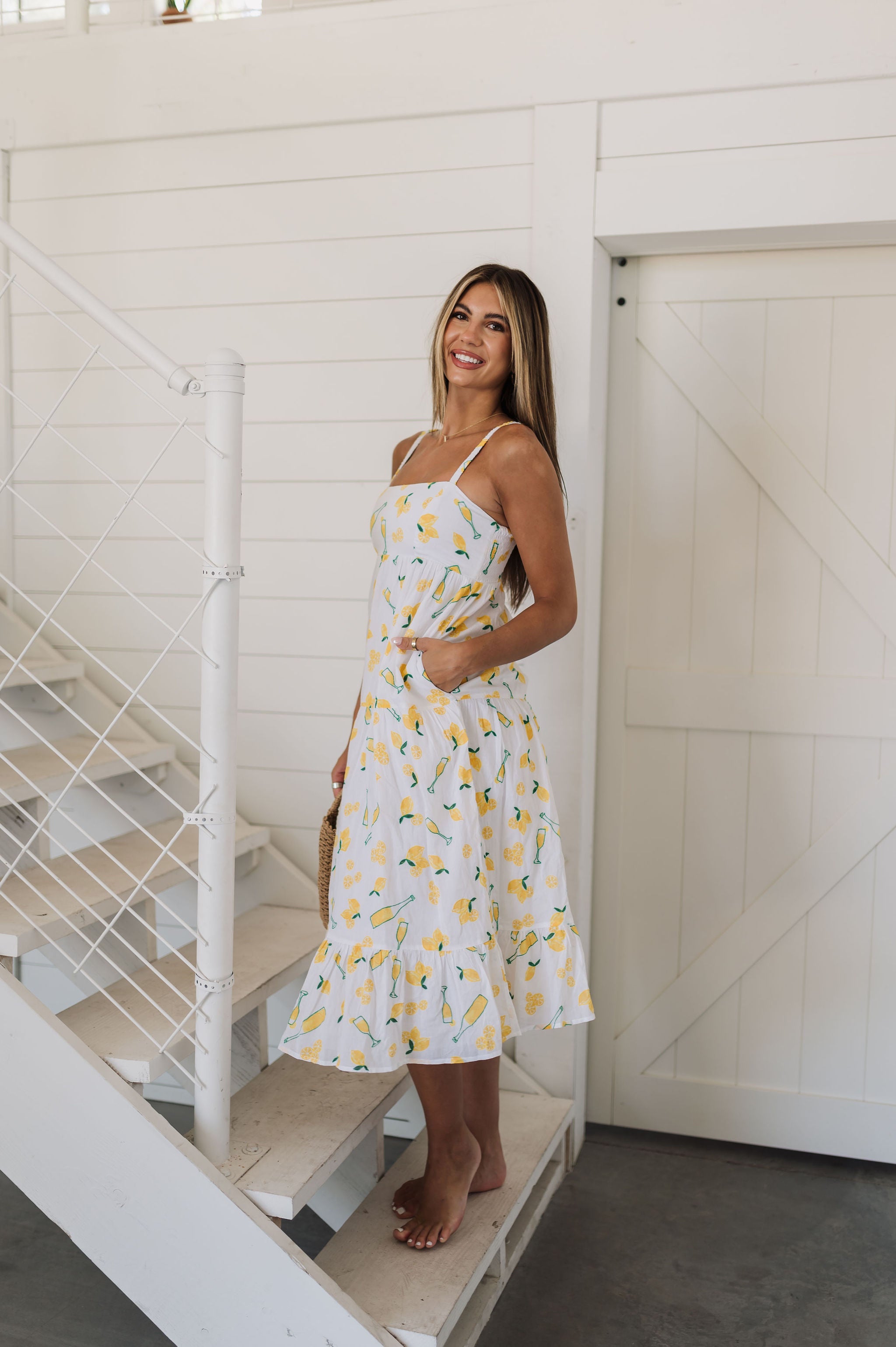 Side view of Summer Fling Midi Dress with embroidered Limoncello print, thin straps, square neckline, side pockets, and ruffled hem.