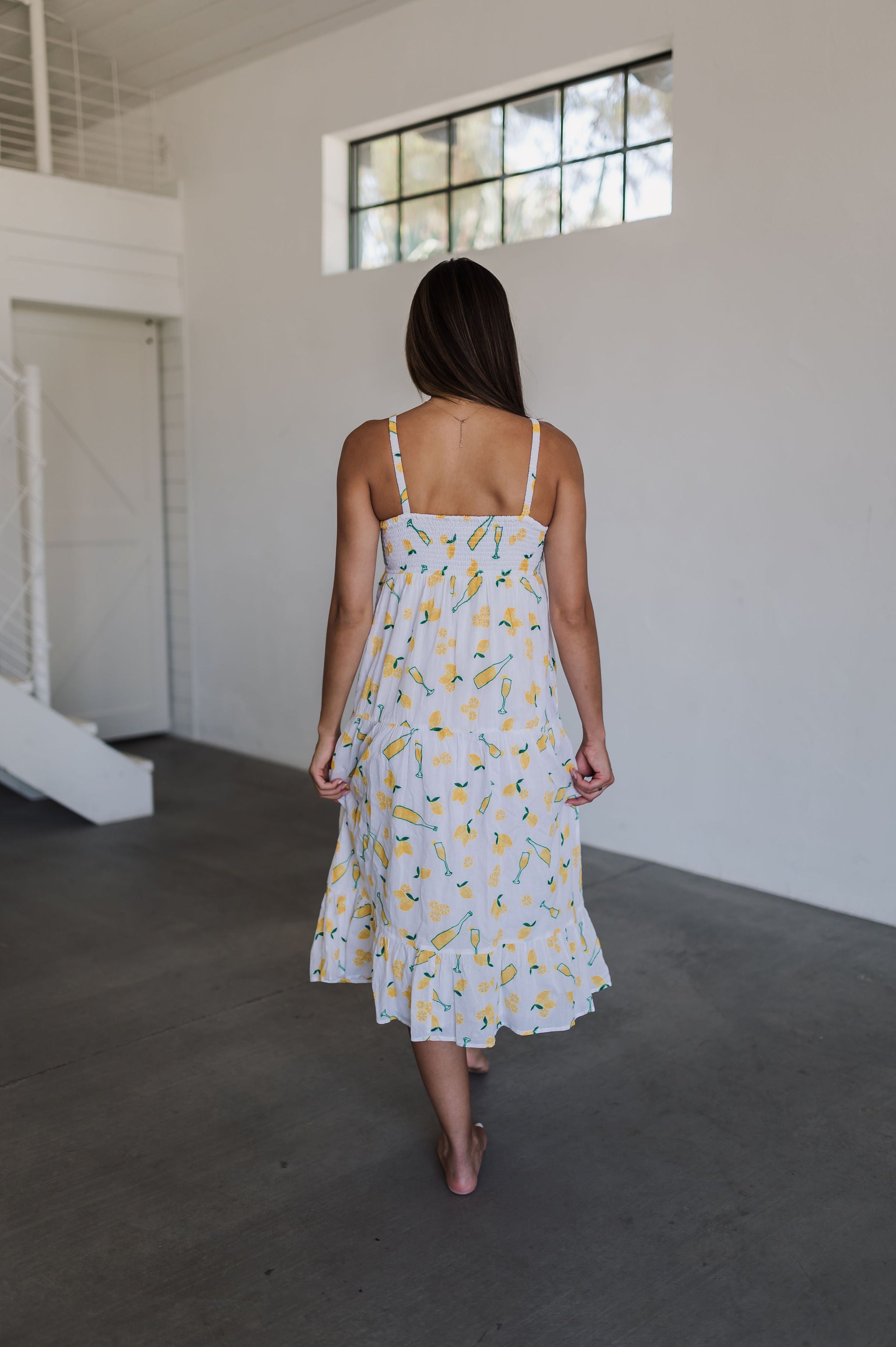 Rear view of Summer Fling Midi Dress with embroidered Limoncello print, thin straps, smocked back, and ruffled hem.