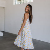 Side view of Summer Fling Midi Dress with embroidered Limoncello print, thin straps, square neckline, side pockets, and ruffled hem.