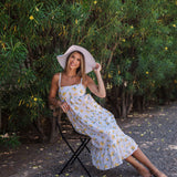 Seated view of Summer Fling Midi Dress with embroidered Limoncello print, thin straps, square neckline, and ruffled hem. 