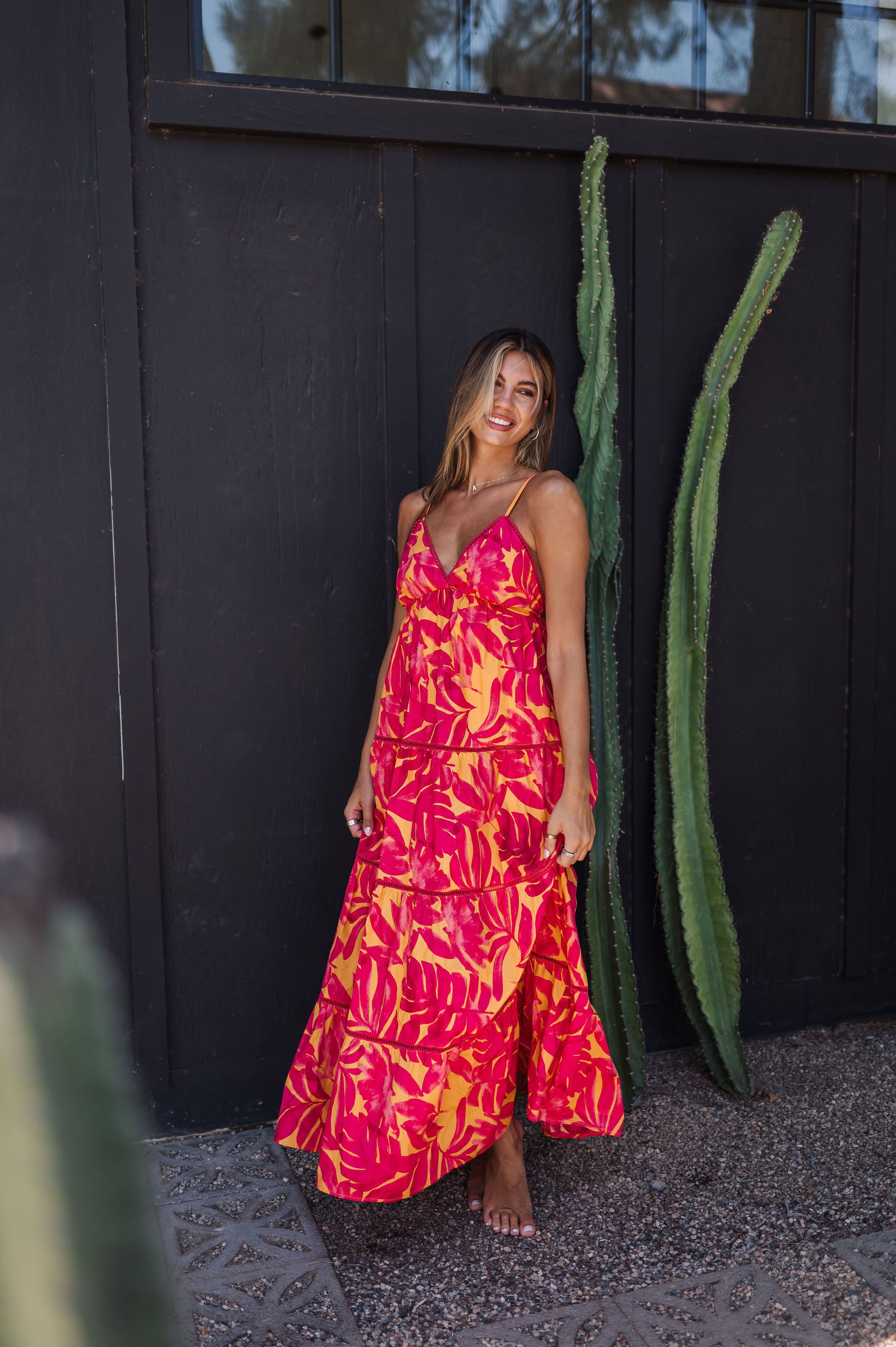 Front angled view of Amalfi Sunset Maxi Dress with thin straps, deep V-neck, allover neon print, and lace trim. 