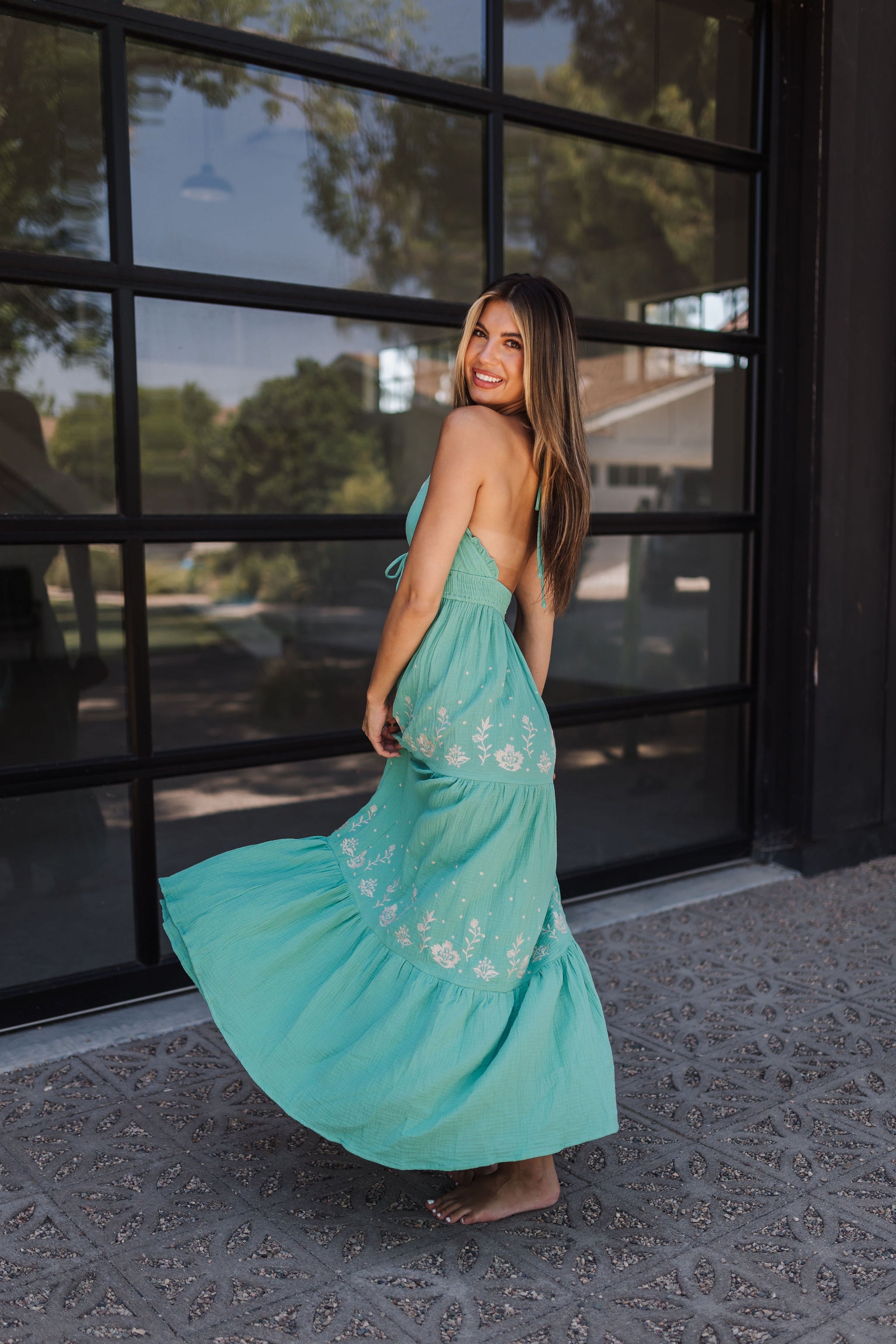 Side view of Azure Floral Embroidered Maxi Dress with floral embroidered details, ruffle hem, halter neckline, and open back.