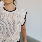 Close up front view of pointelle knit Piper Knit Top with ruffled sleeve and hem and contrast piping detail. 