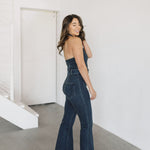 Side view of Fort Worth Jumpsuit in blue with belted waist, embroidered rear pocket, halter top, and flared leg. 