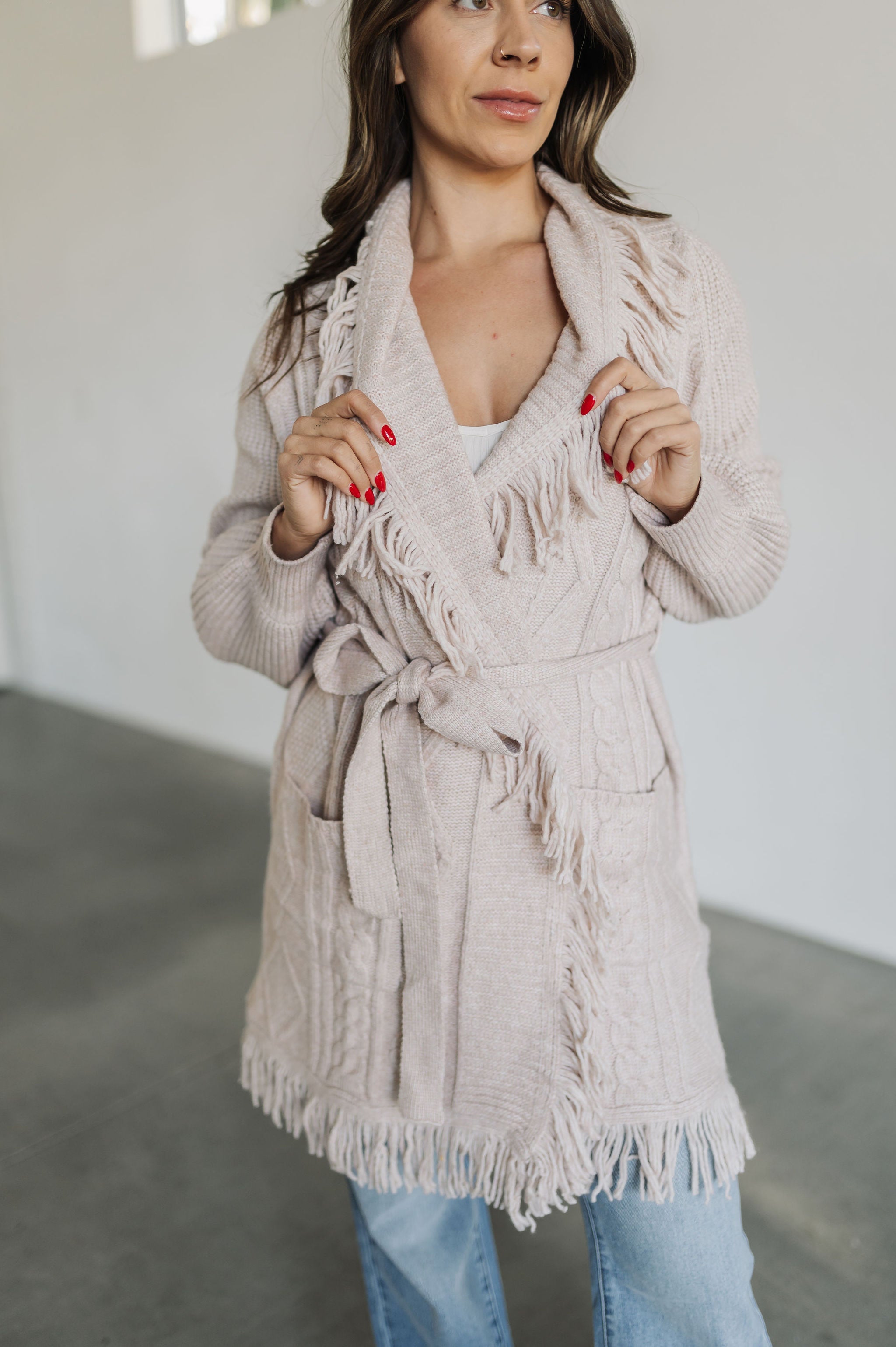 Front view of cream knit Freya Cardigan with belt tie closure, front pockets, and fringe trim. 