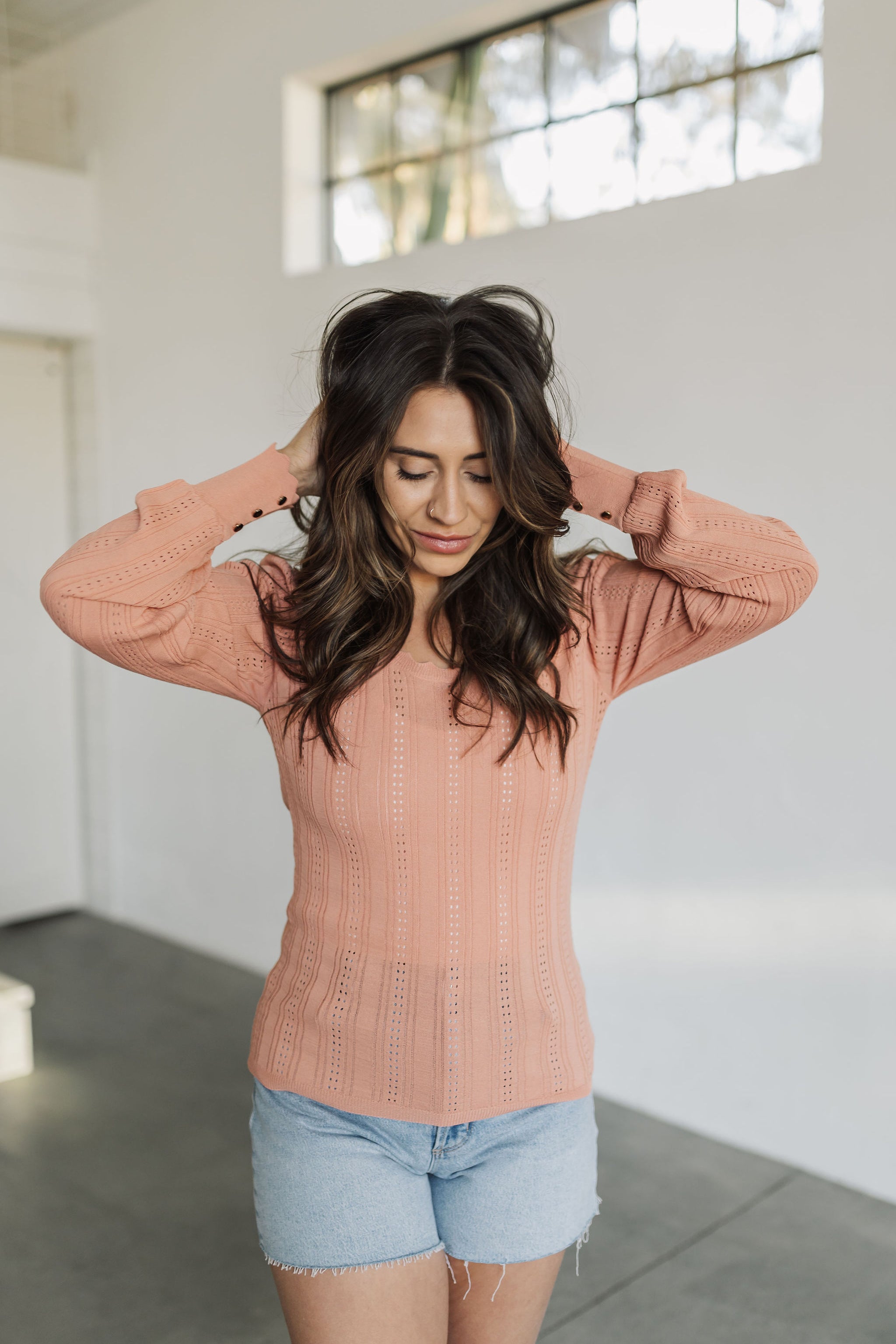 Close up front view of salmon colored Daphne Pointelle Knit Sweater Top with scalloped edges and buttoned sleeves. 