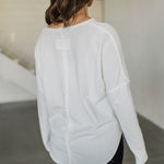 Rear angled view of Harper Long Sleeve Top with notch neckline and raw hem. 