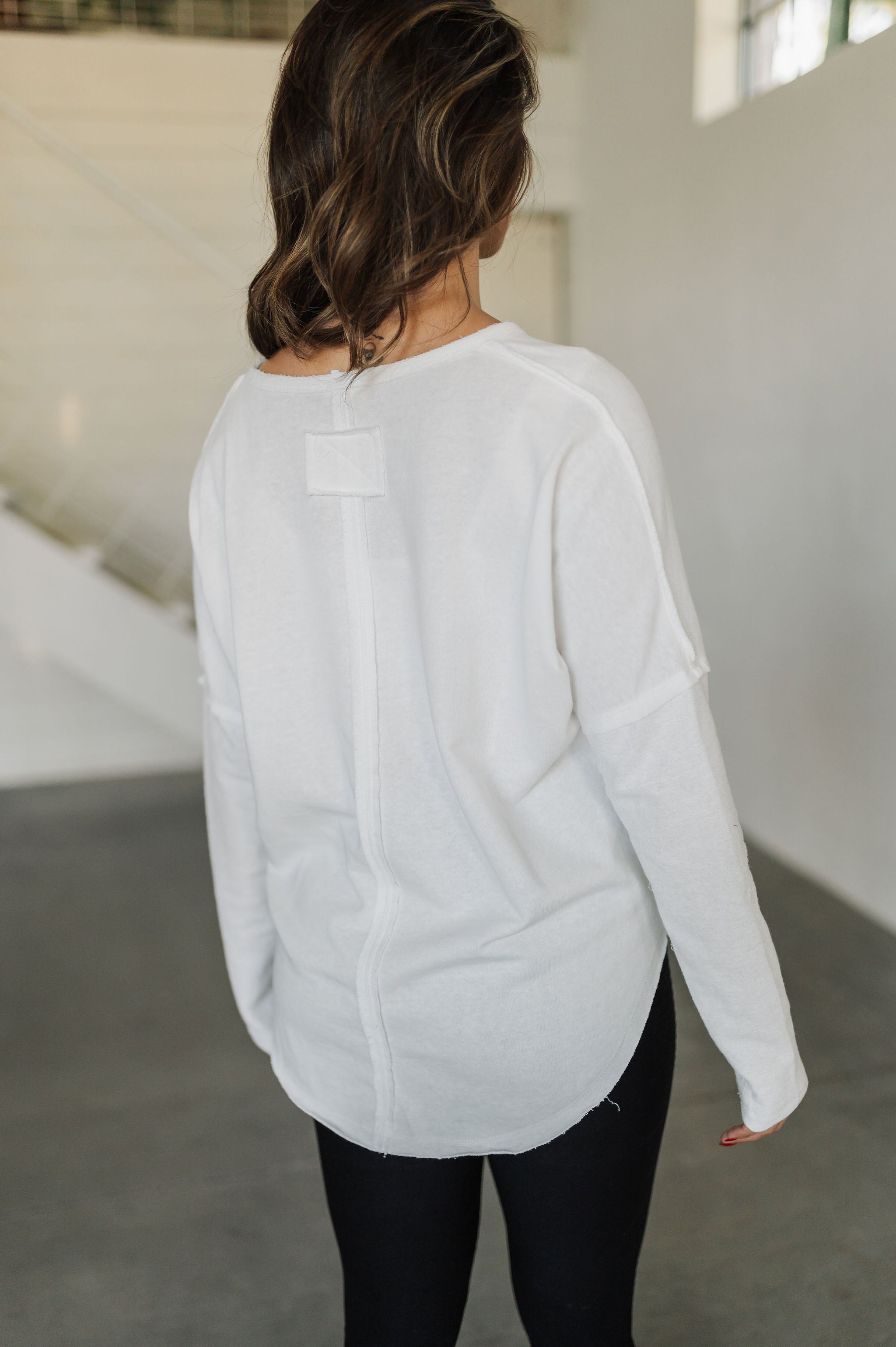Rear angled view of Harper Long Sleeve Top with notch neckline and raw hem. 