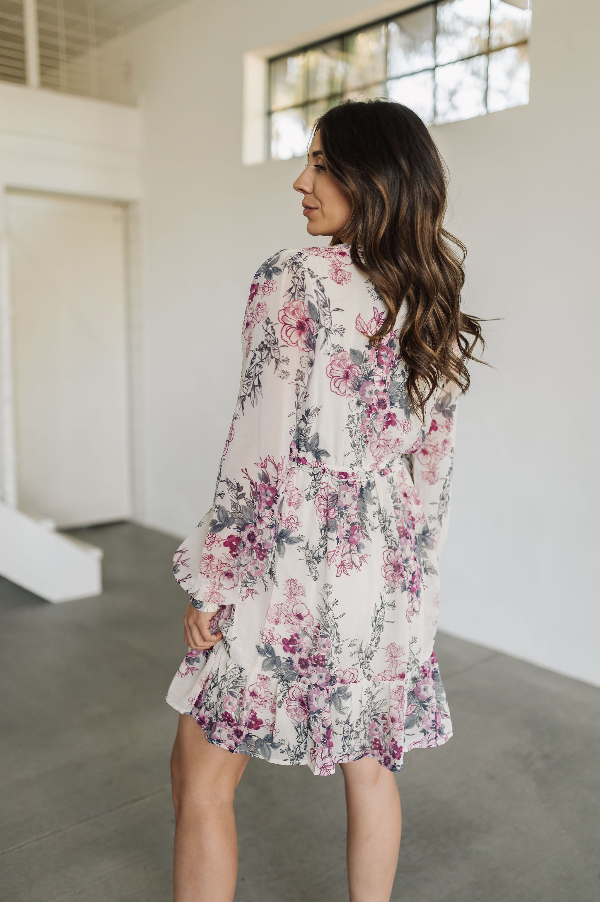 Angled rear view of Aster Floral Mini Dress with long sleeves and ruffled hem. 