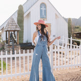 Front view of Clementine Wide Leg Distressed Denim Overalls with raw hem and front and side pockets.