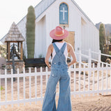 Rear view of Clementine Wide Leg Distressed Denim Overalls with raw hem and back pockets. 