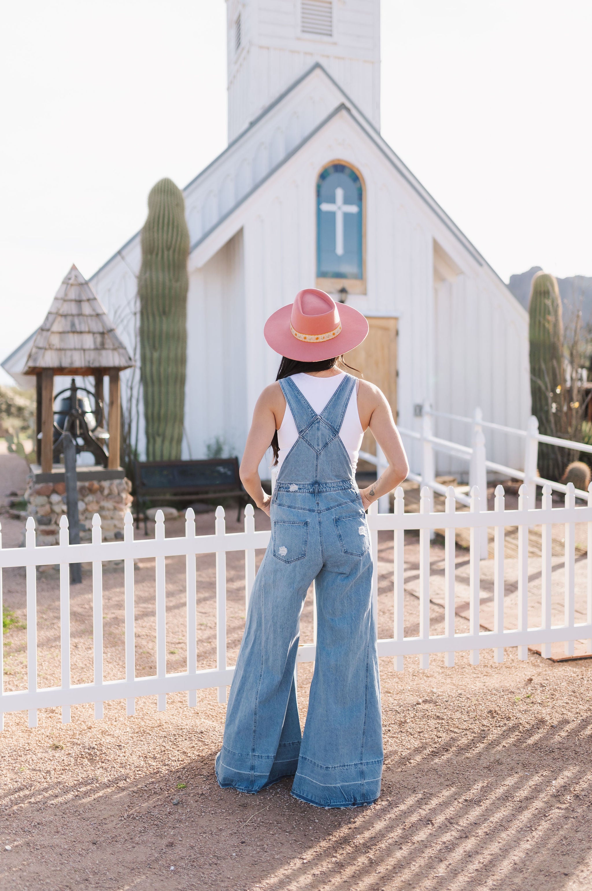 Rear view of Clementine Wide Leg Distressed Denim Overalls with raw hem and back pockets. 