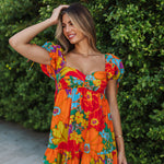 Front view of Paradise Blossom Mini Dress with allover bright tropical print, puff sleeves with ties, bustier top, and ruffle hem. 