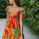 Front view of Paradise Blossom Mini Dress with allover bright tropical print, puff sleeves with ties, bustier top, and ruffle hem. 