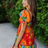 Side view of Paradise Blossom Mini Dress with allover bright tropical print, puff sleeves with ties, smocked back, and ruffle hem. 