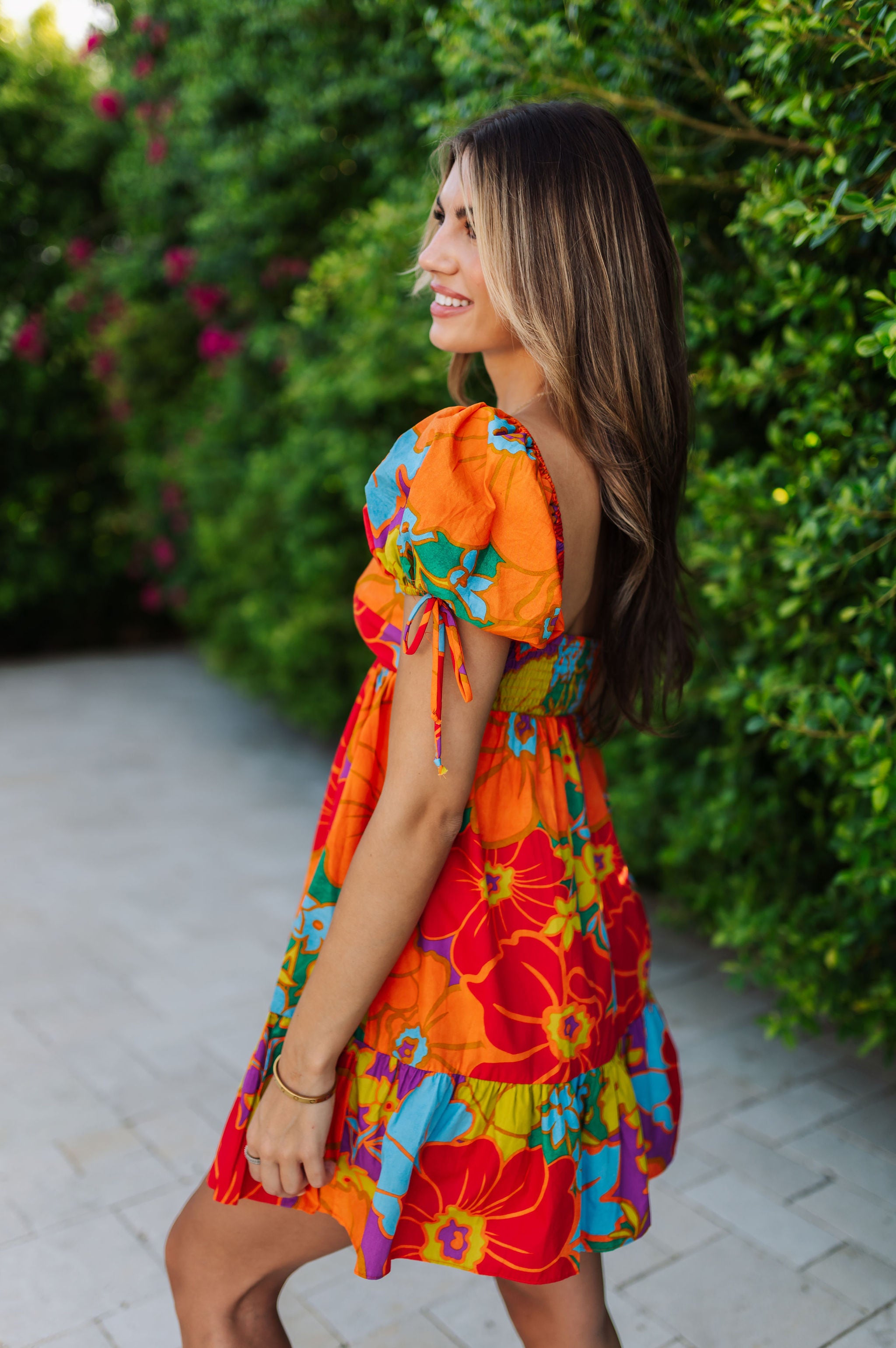 Side view of Paradise Blossom Mini Dress with allover bright tropical print, puff sleeves with ties, smocked back, and ruffle hem. 