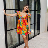 Front view of Paradise Blossom Mini Dress with allover bright tropical print, puff sleeves with ties, bustier top, and ruffle hem. 