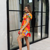 Side view of Paradise Blossom Mini Dress with allover bright tropical print, puff sleeves with ties, bustier top, and ruffle hem. 