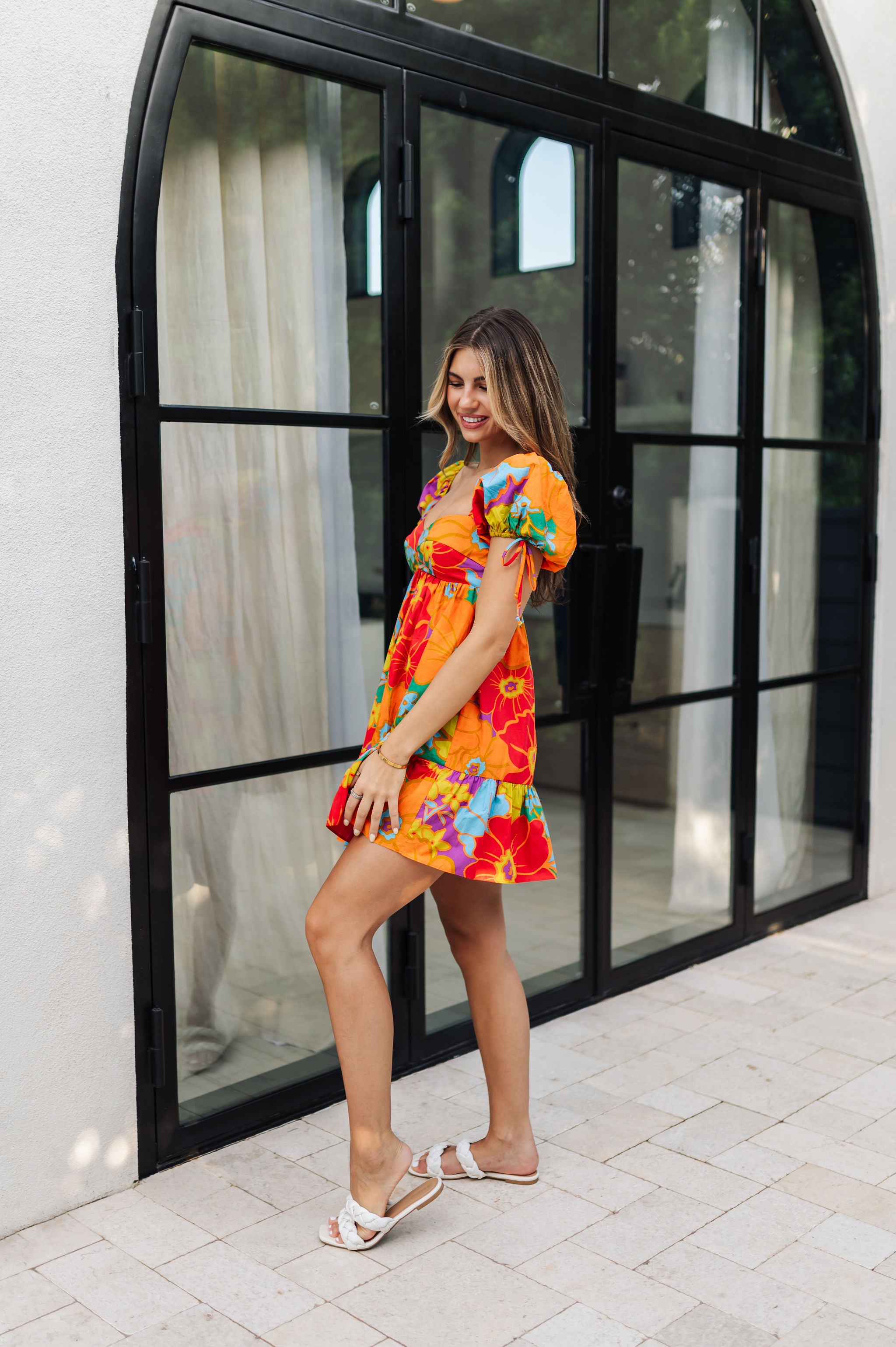 Side view of Paradise Blossom Mini Dress with allover bright tropical print, puff sleeves with ties, bustier top, and ruffle hem. 