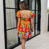 Rear view of Paradise Blossom Mini Dress with allover bright tropical print, puff sleeves with ties, smocked back, and ruffle hem. 