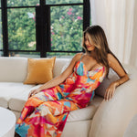 Front seated view of Golden Hour Jumpsuit in bright water color print, thin straps, and a bustier top. 