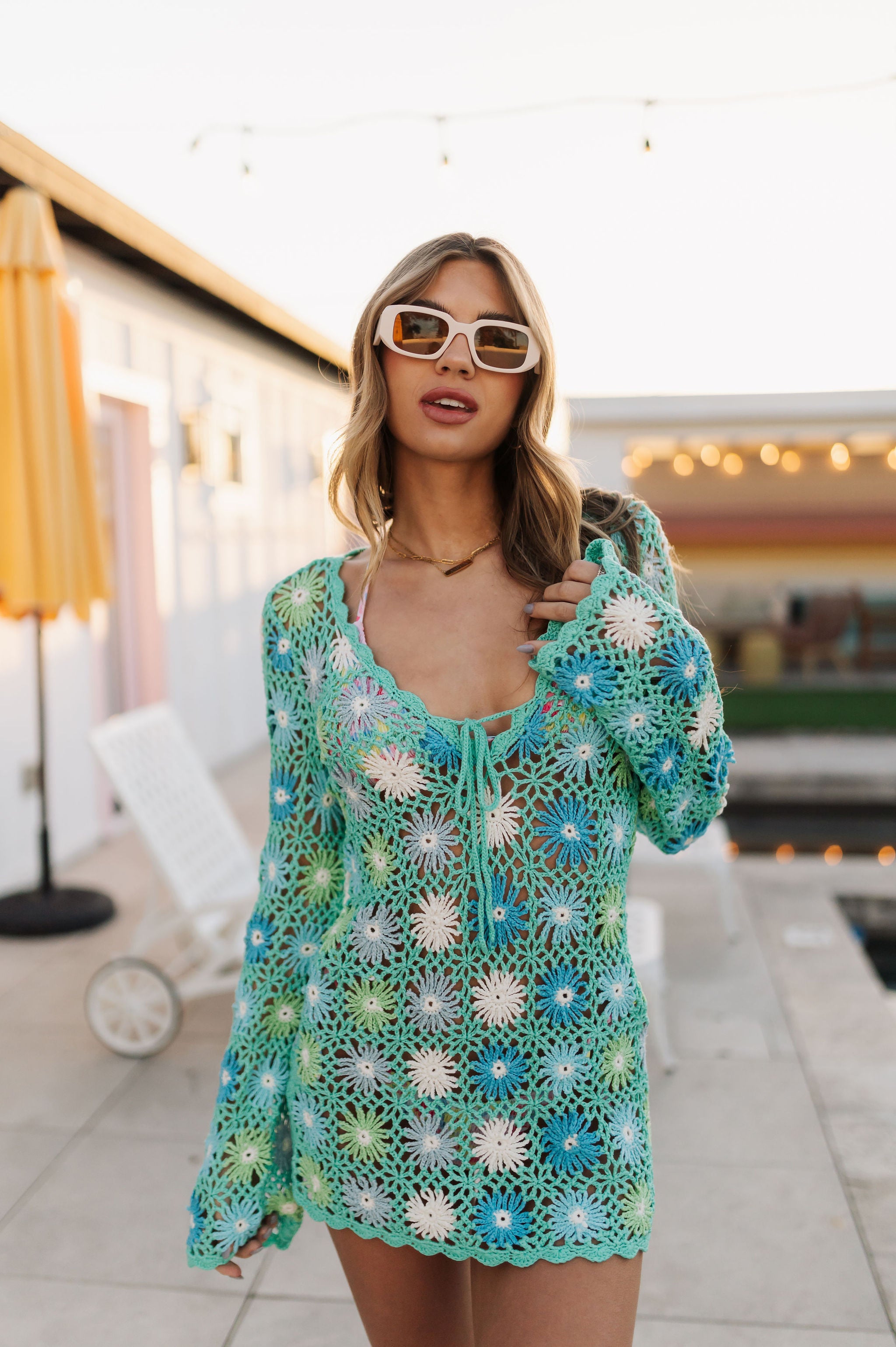 Close up front view of floral patchwork crochet Vacay Mini Coverup with long sleeves, scalloped edges, deep V neckline, and tie front.