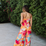 Rear view of Golden Hour Jumpsuit in bright water color print, thin straps, and wide legs. 