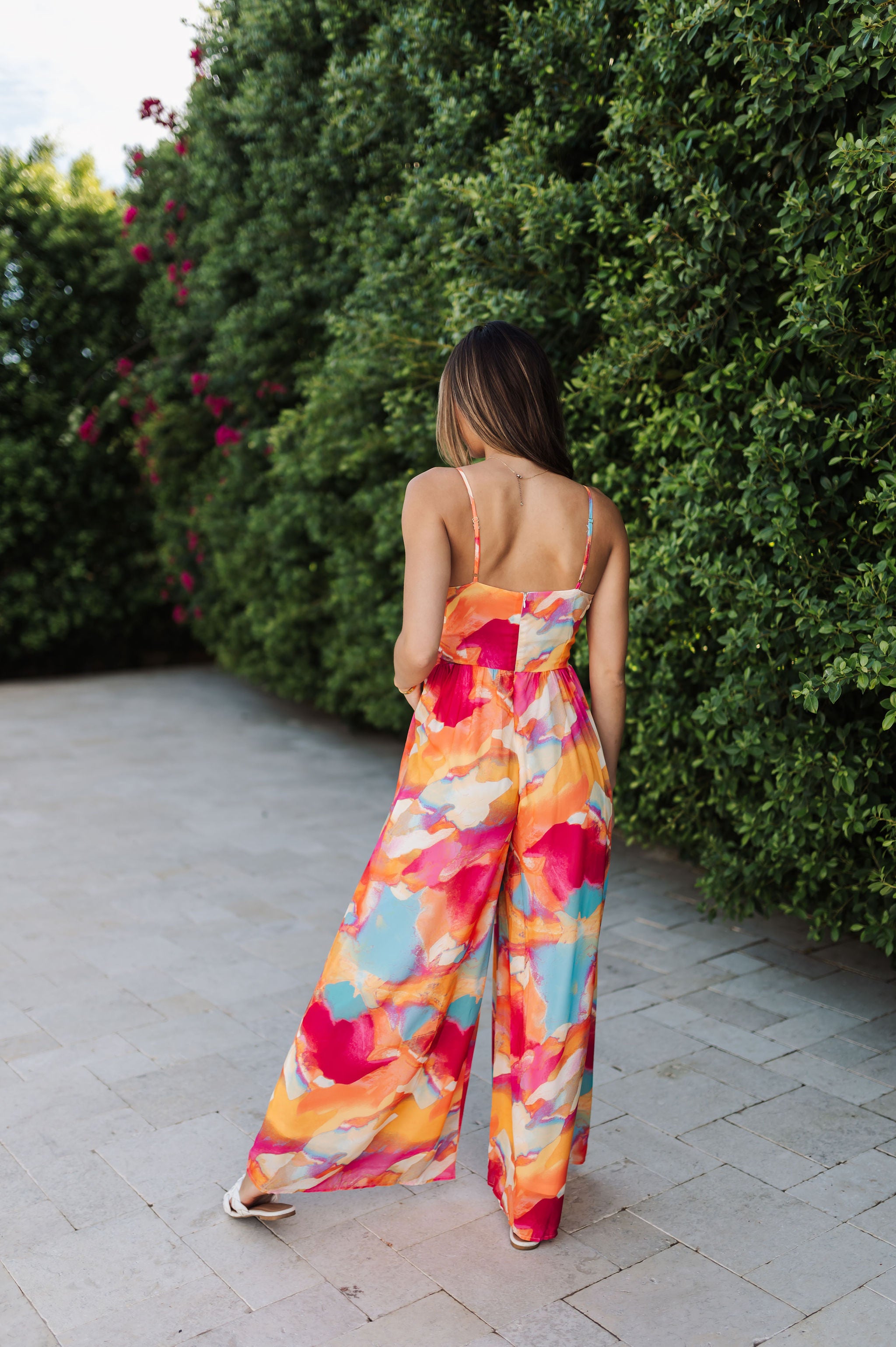 Rear view of Golden Hour Jumpsuit in bright water color print, thin straps, and wide legs. 