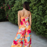 Rear view of Golden Hour Jumpsuit in bright water color print, thin straps, and wide legs. 