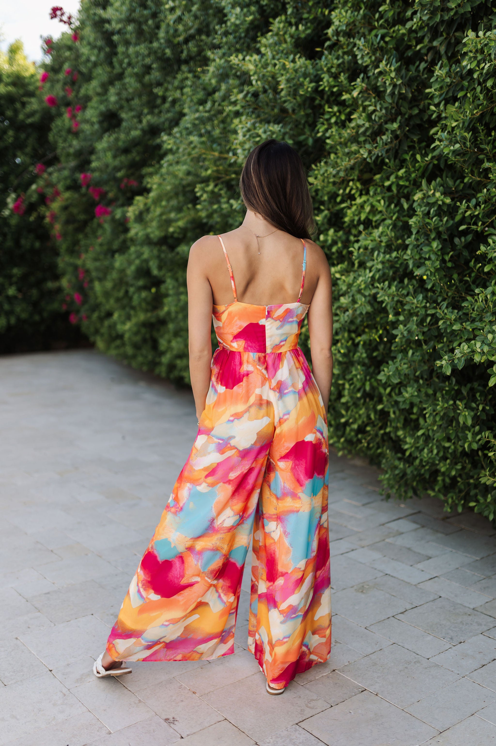 Rear view of Golden Hour Jumpsuit in bright water color print, thin straps, and wide legs. 