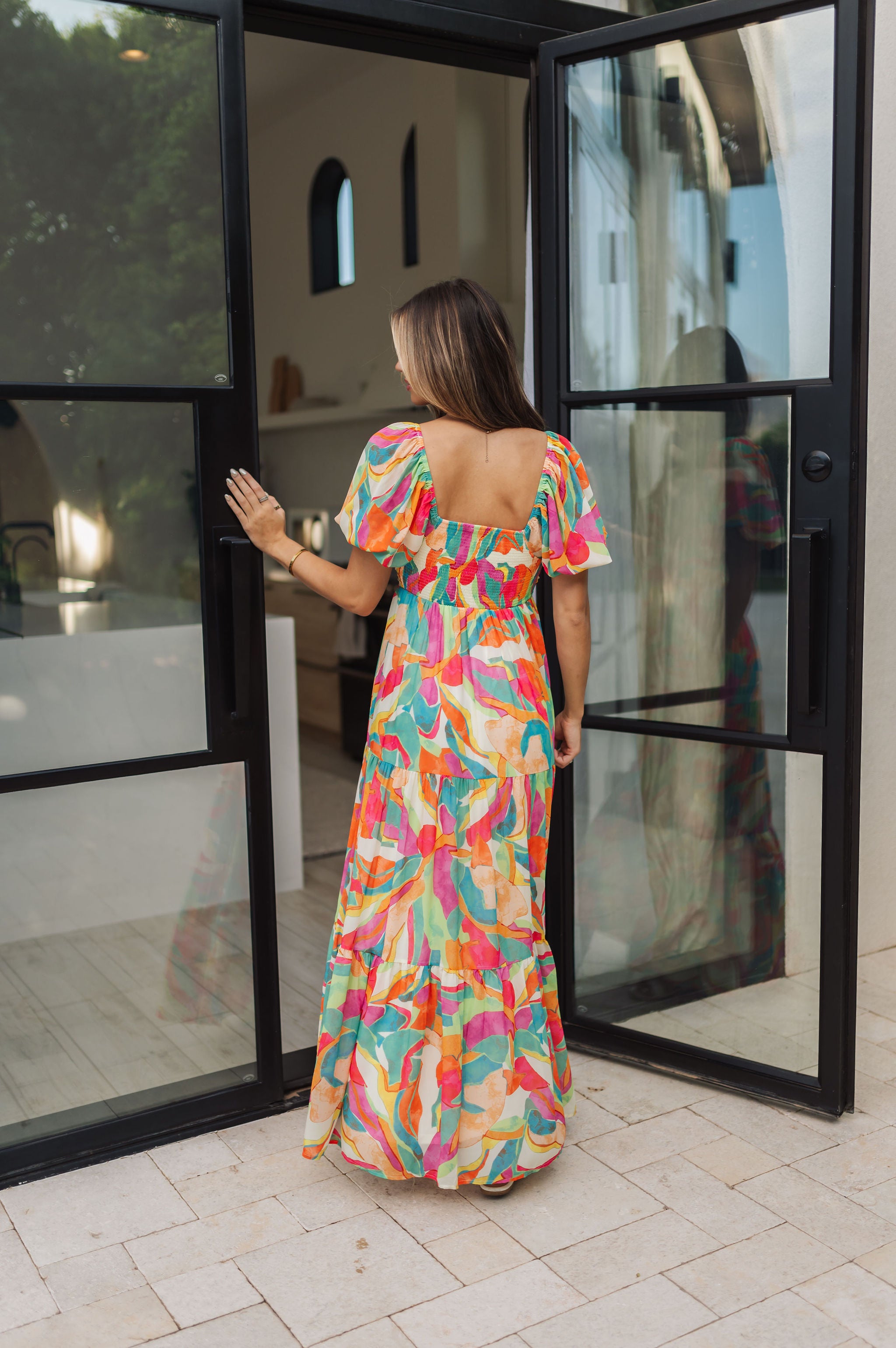 Rear view of  Isle Glow Maxi Dress in allover bright floral print with short puff  sleeves, smocked back, and ruffle hem. 